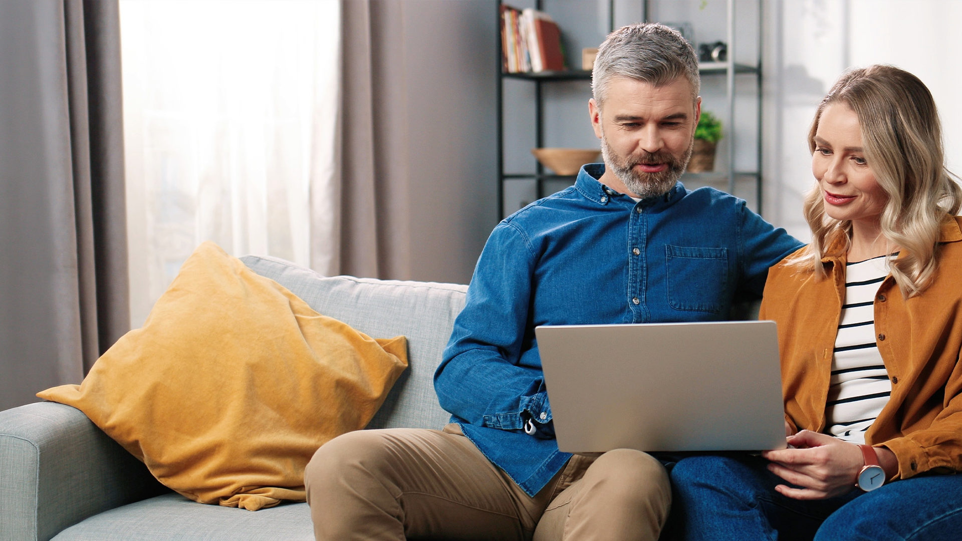 Middle aged couple sat on the sofa whilst on a laptop.