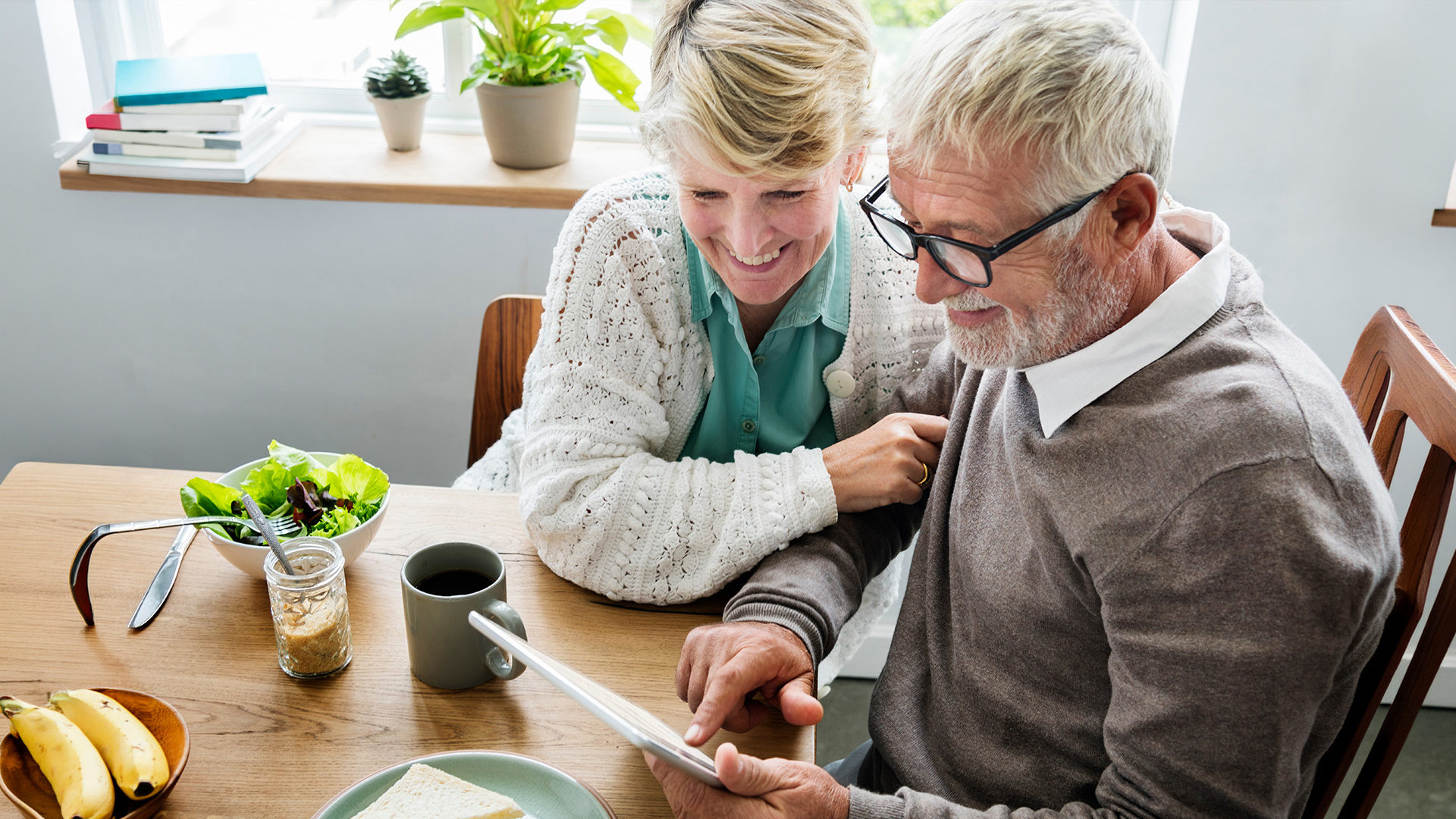 Older couple sitting at a dining table on their tablet device.