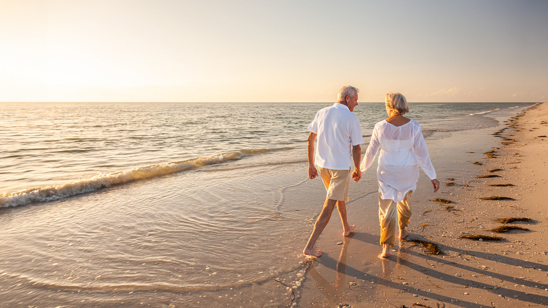 Older couple walking hand in hand at the beach.