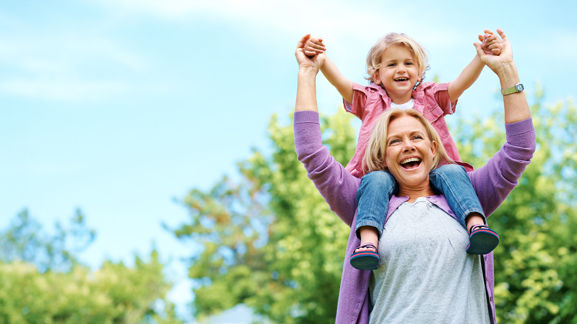 Older woman with their grandchild on their shoulders smiling.