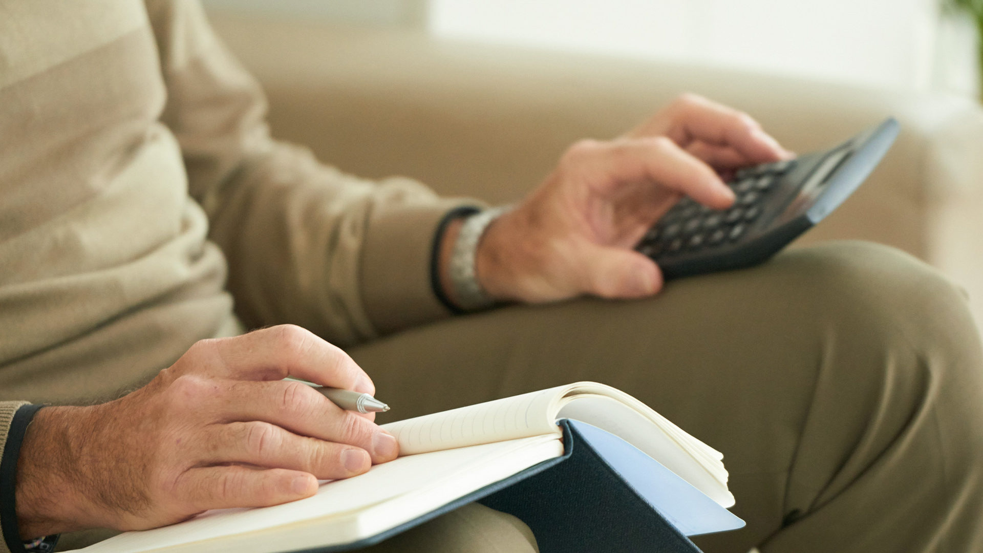 Older man with a notebook and calculator on his lap.